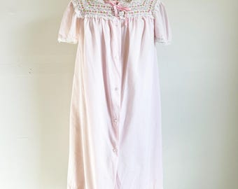 May include: A pink cotton nightgown with a lace trim and floral embroidery. The gown has a button-up front and short sleeves.