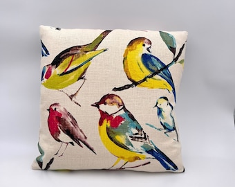 May include: A cream-colored throw pillow with a colorful bird pattern. The birds are painted in shades of yellow, blue, red, and green. The pillow is made of a soft, textured fabric.