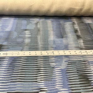 May include: Blue and black fabric with a wavy, abstract pattern. A ruler is placed on top of the fabric to show the scale.