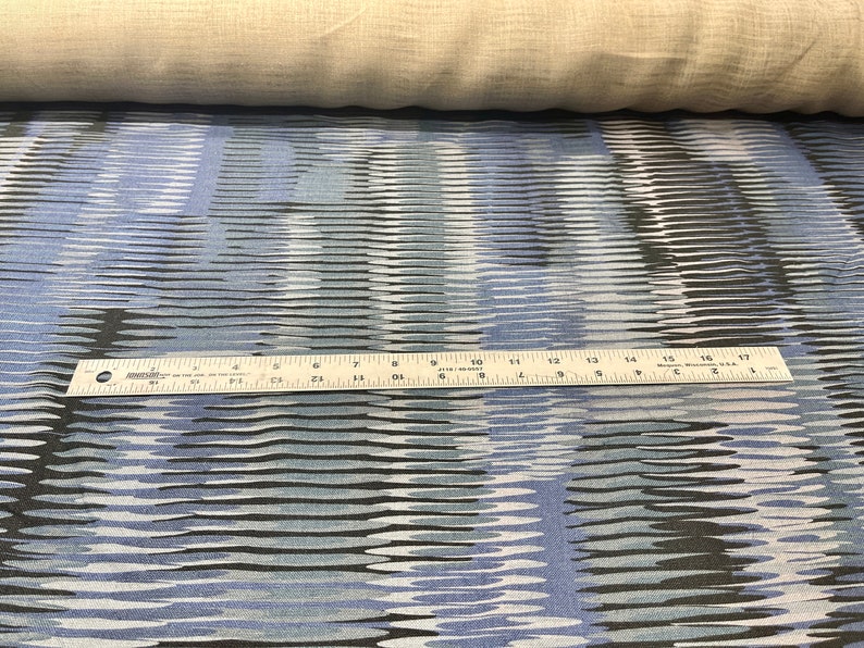 May include: Blue and black fabric with a wavy, abstract pattern. A ruler is placed on top of the fabric to show the scale.