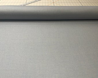 May include: A roll of light gray fabric. The fabric is a solid color and appears to be a medium weight material. The fabric is rolled up, and the end of the roll is visible. A ruler is in the background.