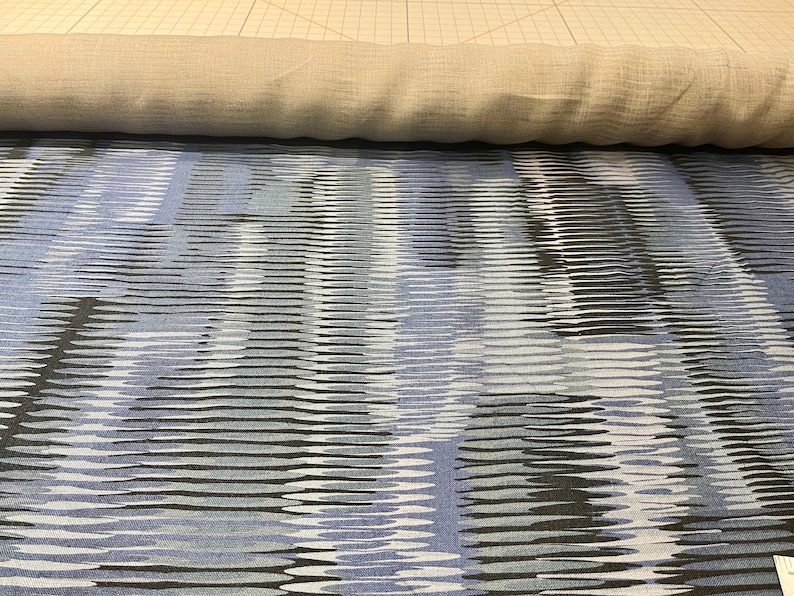May include: A close-up of a blue and white patterned fabric with a subtle wave design. The fabric is rolled up and has a light brown color on the underside.
