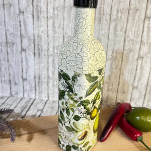 May include: A white ceramic bottle with a black lid and a crackled finish. The bottle is decorated with a botanical print featuring avocados, lemons, and leaves.