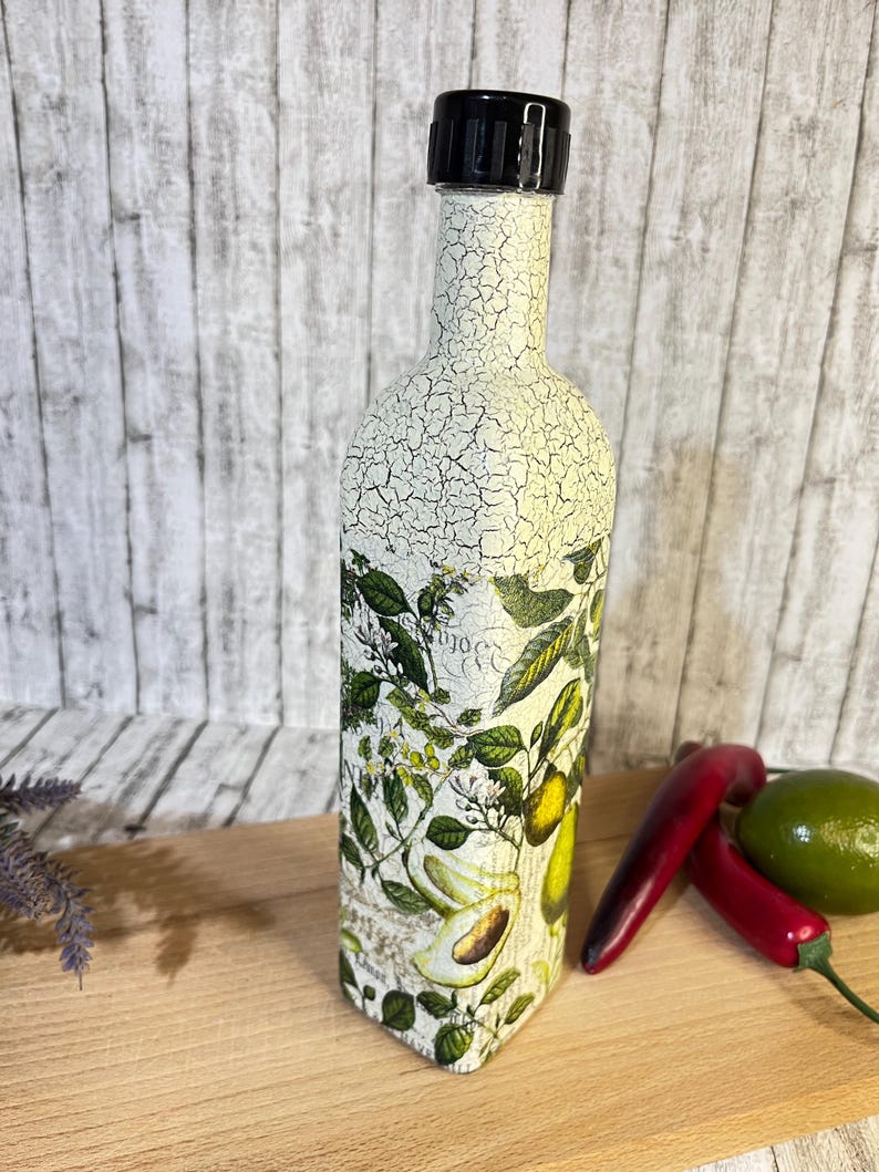 May include: A white ceramic bottle with a black lid and a crackled finish. The bottle is decorated with a botanical print featuring avocados, lemons, and leaves.