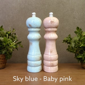 May include: Two wooden salt and pepper shakers, one painted sky blue and the other baby pink. The shakers have a distressed finish and are standing on a wooden surface. "Sky blue - Baby pink" is written below the shakers.