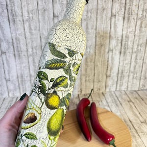 May include: A white ceramic bottle with a black lid, decorated with a vintage botanical print of lemons, avocados, and leaves. The bottle is cracked and distressed, giving it a rustic look.