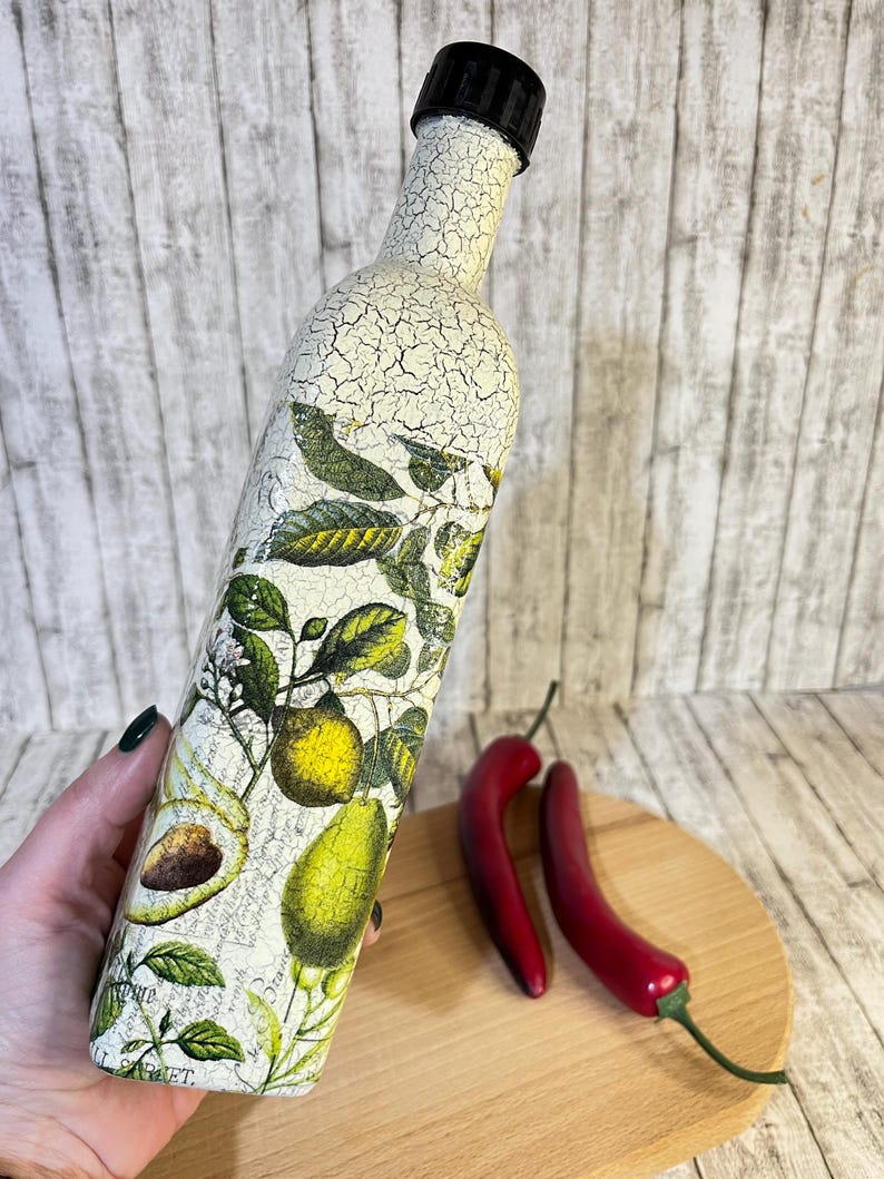 May include: A white ceramic bottle with a black lid, decorated with a vintage botanical print of lemons, avocados, and leaves. The bottle is cracked and distressed, giving it a rustic look.