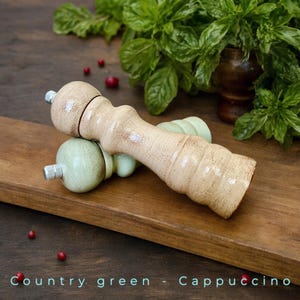 May include: Two wooden salt and pepper shakers. One is a light brown color with a distressed finish and the other is a light green color with a distressed finish. The shakers are sitting on a wooden surface.