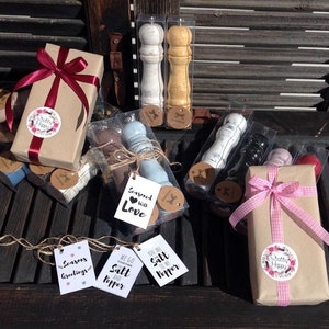 Puede incluir: Una colecci&oacute;n de saleros y pimenteros empaquetados en cajas de pl&aacute;stico transparente con papel de regalo marr&oacute;n y cinta rosa y roja. Las cajas est&aacute;n atadas con cuerda y tienen etiquetas de regalo con varios lemas, incluyendo "Sazonados con amor", "Vamos juntos como la sal y la pimienta" y "Eres la sal de mi pimienta".
