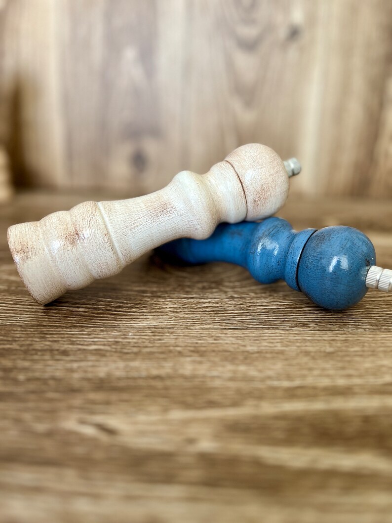 Puede incluir: Dos saleros y pimenteros, uno blanco y otro azul, sobre una superficie de madera.