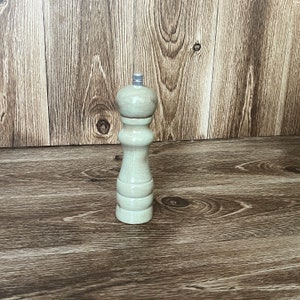 May include: A wooden salt and pepper grinder with a light brown finish. The grinder has a simple design and a silver top.