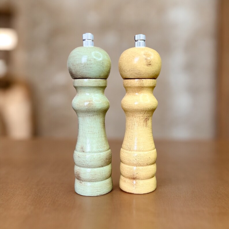 May include: Two wooden salt and pepper shakers, one is green and the other is yellow. They are both distressed and have a rustic look.