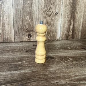 May include: A wooden salt and pepper grinder with a light brown finish. The grinder has a metal top and a round body.