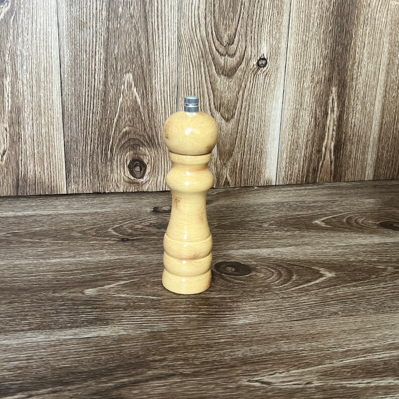 May include: A wooden salt and pepper grinder with a light brown finish. The grinder has a metal top and a round body.