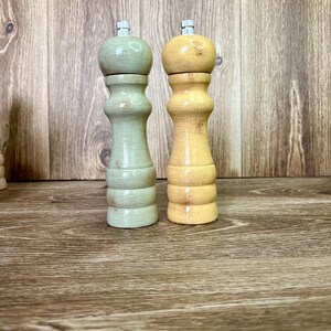 May include: Two wooden salt and pepper shakers, one green and one yellow, on a wood surface.