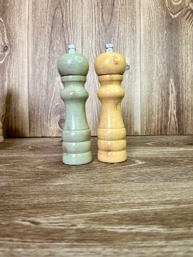 May include: Two wooden salt and pepper shakers, one green and one yellow, on a wood surface.