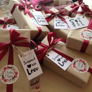 May include: Multiple brown paper gift boxes tied with red ribbon and decorated with tags that say "Seasoned with Love" and "Shabby Happy".