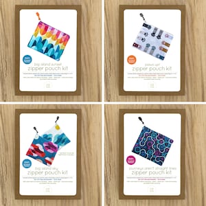 Op de afbeelding: Vier verschillende rits-tassets met kleurrijke stoffenontwerpen. Elke set bevat alle benodigde materialen om een kleine rits-tas te maken van 18 cm x 18 cm. De ontwerpen omvatten "Big Island Sunset", "Paws Up!" , "Big Island Sky" en "Journeys Aren't Straight Lines".