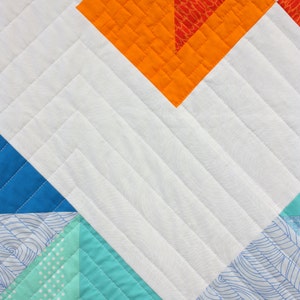 K&ouml;nnte beinhalten: Eine Steppdecke mit einem geometrischen Muster in Blaut&ouml;nen, Gr&uuml;n, Orange und Wei&szlig;. Die Steppdecke ist mit einem geraden Linienmuster gesteppt. Der Text "wholecirclestudio.com" ist in der rechten unteren Ecke sichtbar.