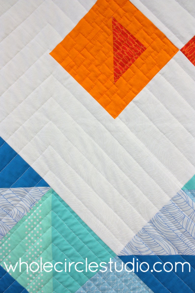 K&ouml;nnte beinhalten: Eine Steppdecke mit einem geometrischen Muster in Blaut&ouml;nen, Gr&uuml;n, Orange und Wei&szlig;. Die Steppdecke ist mit einem geraden Linienmuster gesteppt. Der Text "wholecirclestudio.com" ist in der rechten unteren Ecke sichtbar.