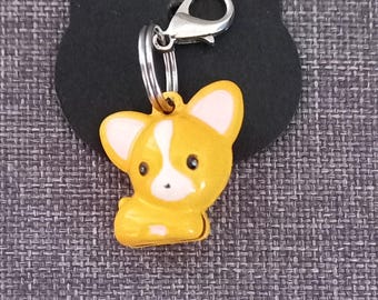 May include: A yellow and white cartoon dog charm with a silver key ring. The charm is attached to a black background.
