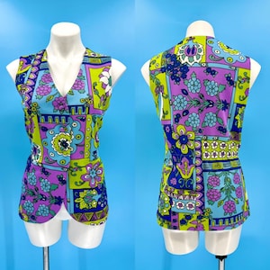 May include: A vintage sleeveless top with a vibrant floral pattern in shades of purple, blue, green, and white. The top features a V-neck and a unique, retro design, showcasing a bold, colorful aesthetic. The garment is displayed on a mannequin.