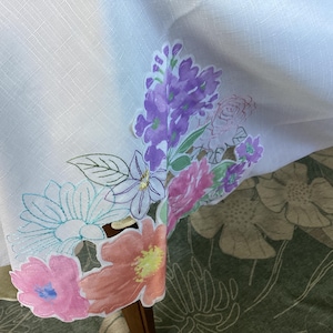 May include: White tablecloth with embroidered floral design. The design features pink, purple, and green flowers with white outlines.