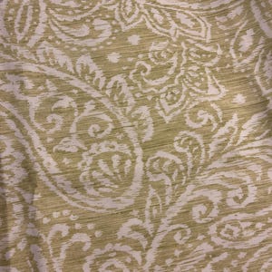 May include: A fabric featuring a repeating paisley pattern in shades of olive green and white. The design consists of intricate, swirling teardrop shapes and floral motifs set against a textured background, creating a dense, continuous visual pattern.