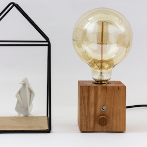 Op de afbeelding: Een houten tafellamp met een grote, heldere glazen lamp. De lamp heeft een eenvoudig, modern ontwerp en is perfect voor een minimalistisch huis.