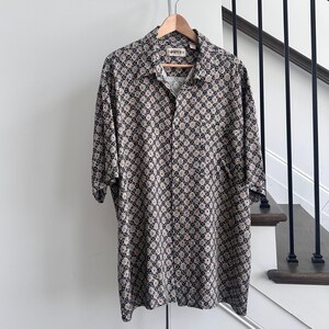 Puede incluir: Una camisa de manga corta con botones, cuello y estampado negro y beige.