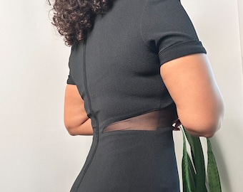 May include: Black short-sleeved dress with a mesh panel detail on the side. The dress has a fitted silhouette and a high neckline.