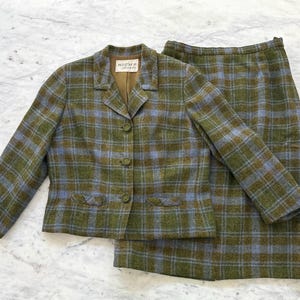 May include: A vintage two-piece suit in a green, blue, and brown plaid pattern. The jacket has a notched collar, three buttons, and two front pockets. The matching skirt is a pencil skirt. The jacket label reads "High's".