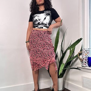 May include: A woman wearing a black crop top with a white graphic print and a pink floral skirt. The skirt has a ruffled hem and a drawstring detail.