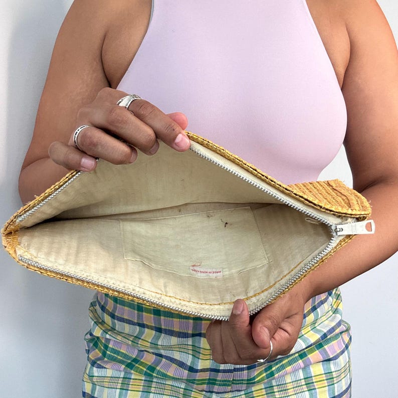May include: A yellow woven clutch with a zipper closure and a white fabric lining. The clutch has a small pocket inside and a label that reads "Made in Japan".
