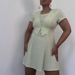 May include: A light green dress with a white embroidered vest-like bodice. The dress has a short-sleeved, A-line silhouette.