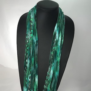 May include: A green and turquoise silk scarf with a shimmery finish. The scarf is draped over a black mannequin.