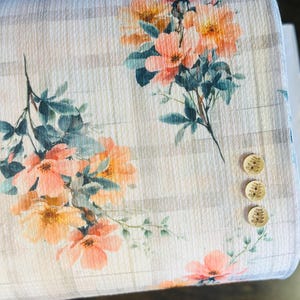 Peut inclure: Gros plan sur un tissu floral avec des fleurs de pêches et d'oranges et des feuilles turquoise. Le tissu présente un motif rayé et trois boutons en bois. Idéal pour les vêtements ou la décoration intérieure.