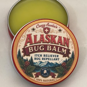 Puede incluir: Una lata metálica redonda que contiene un bálsamo de color verde claro. La tapa presenta el texto Crazy Auntie's ALASKAN BUG BALM, ITCH RELIEVER BUG REPELLANT y 100% NATURAL. El diseño incluye un paisaje montañoso, pinos y un mapa de Alaska.