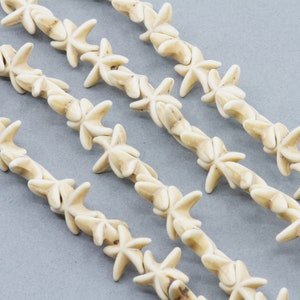 May include: Off-white starfish-shaped beads strung together in a row. The beads are arranged in a diagonal pattern against a gray background. The starfish beads have a natural, organic appearance.