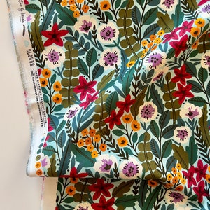 May include: Floral fabric with a light blue background, featuring a dense pattern of red, white, purple, and yellow flowers, along with green and brown leaves. The fabric has a white selvage edge with text.