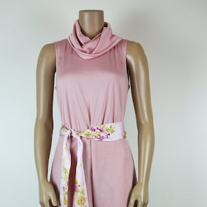 May include: A pink jumpsuit with a cowl neck and wide legs. A floral patterned scarf is tied around the waist as a belt.