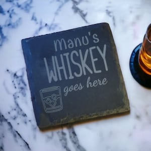 May include: Black slate coaster with the text "Manu's Whiskey goes here" and a small illustration of a glass of whiskey with ice cubes.