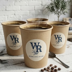 May include: Four paper coffee cups filled with dark coffee, each with a circular label featuring the letters "WR" and the text "ARTISANAL COFFEE | EST. 2024". A spoon and coffee beans are on the wooden table.