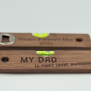 May include: Two wooden bottle openers with engraved text. One says "Happy Father's Day 2025" and has a bottle opener. The other says "MY DAD is next level awesome". Both have a level bubble.