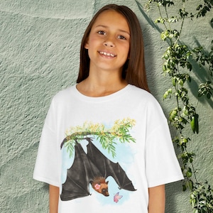 May include: White t-shirt with a watercolour illustration of a bat hanging from a flowering branch. The bat is black with a brown face and a pink flower. A pink butterfly is also present.