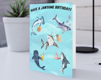 May include: A blue birthday card with the text "Have a Jawsome Birthday!" and illustrations of sharks, a hammerhead shark, and a birthday cake.
