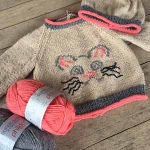 May include: A knitted baby sweater and hat set in beige with a pink and gray trim. The sweater features a cute cartoon mouse design. The set is made with Super Baby yarn by Phildar.
