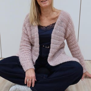 May include: A soft pink cardigan with a loose fit and long sleeves. The cardigan is made of a fuzzy yarn and has a V-neck.