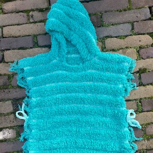 May include: A turquoise hooded poncho with white stripes and frayed edges. The poncho is made of a soft, fuzzy material.