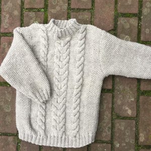 Op de afbeelding: Een grijze kabel gebreide trui met een ronde hals.